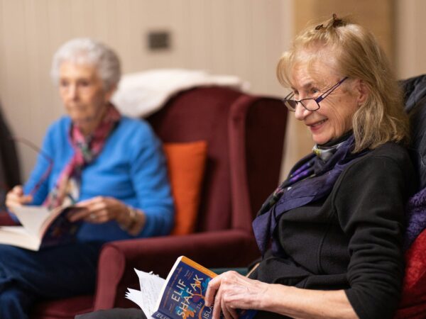 Two older women sitting in chairs reading and discussing a book